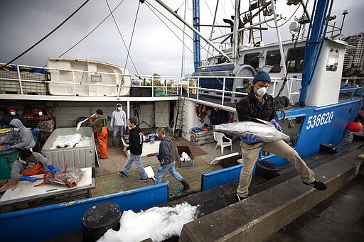 Fishing boat captain Nick Haworth, right, carries tuna to a dock for sale Friday, March 20, 2020, in San Diego. Haworth came home to California after weeks at sea to find a state all but shuttered due to coronavirus measures, and nowhere to sell their catch. A handful of tuna boats filled with tens of thousands of pounds of fish are now floating off San Diego's coast as they scramble to find customers. Haworth was selling on Friday to individuals for less than half what he would get from wholesalers. &quot;This is a quarantine special,&quot; he joked. (AP Photo/Gregory Bull)