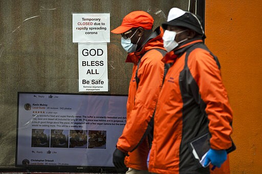 Pedestrians in protective face mask walk past a closed business in Philadelphia, Friday, March 20, 2020. Pennsylvania Gov. Tom Wolf directed all &quot;non-life-sustaining&quot; businesses to close their physical locations late Thursday and said state government would begin to enforce the edict starting early Saturday. (AP Photo/Matt Rourke)