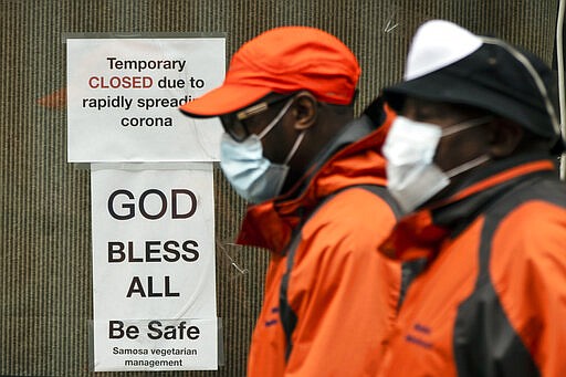 Pedestrians in protective face mask walk past a closed business in Philadelphia, Friday, March 20, 2020. Pennsylvania Gov. Tom Wolf directed all &quot;non-life-sustaining&quot; businesses to close their physical locations late Thursday and said state government would begin to enforce the edict starting early Saturday. (AP Photo/Matt Rourke)