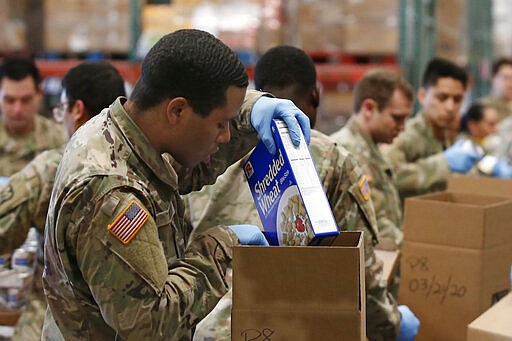 Grant Mock, a PFC with the California National Guard places cereal in a box of food supplies at the Sacramento Food Bank in Sacramento, Calif., Saturday, March 21, 2020. Food banks have been hit hard by a shortage of volunteers due to the mandatory stay-at-home order caused by the coronavirus. Mock and other members of the 115th Regional Support Group are supplementing food bank staff to ensure the food bank continues provide food to those in need. (AP Photo/Rich Pedroncelli)