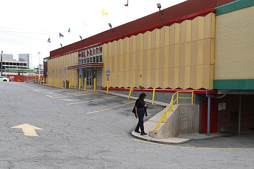 A woman walks across a normally packed parking lot at The Varsity Thursday, March 19, 2020, in Atlanta. The Varsity, known for its chili dogs and onion rings, closed their dining room ahead Atlanta Mayor Keisha Lance Bottoms' order limiting restaurants to takeout only in hopes of slowing the spread of coronavirus. (AP Photo/John Bazemore)