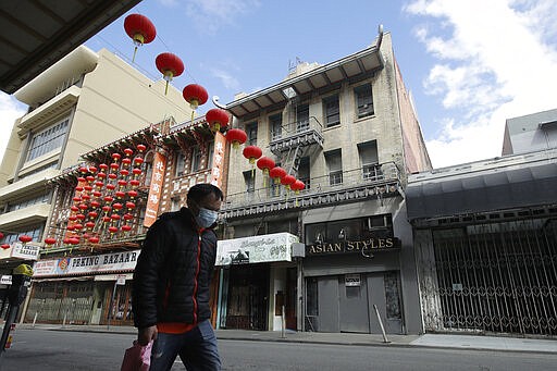 A man wears a mask while walking in front of closed businesses on Grant Avenue in Chinatown in San Francisco, Saturday, March 21, 2020. Some 40 million Californians are coping with their first weekend under a statewide order requiring them to stay at home to help curb the spread of the coronavirus.(AP Photo/Jeff Chiu)