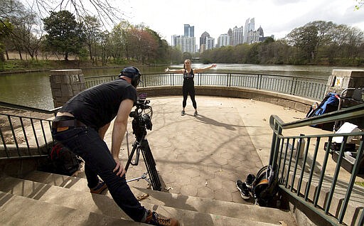 Orangetheory workout instructor Julia Crosby films a 30-minute home workout session for people to use to stay fit while they are practicing social distancing due to the coronavirus, in Piedmont Park on Thursday, March 19, 2020, in Atlanta. (Steve SchaeferAtlanta Journal-Constitution via AP)