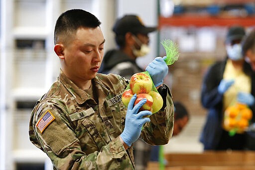 Sgt. Caleb Lim, of the California National Guard ties up a bag of apples at the Sacramento Food Bank and Family Services in Sacramento, Calif., Saturday, March 21, 2020. Food banks have been hit hard by a shortage of volunteers due to the mandatory stay-at-home order caused by the coronavirus. Lim and other members of the 115th Regional Support Group are supplementing food bank staff to ensure the food bank continues provide food to those in need.(AP Photo/Rich Pedroncelli)