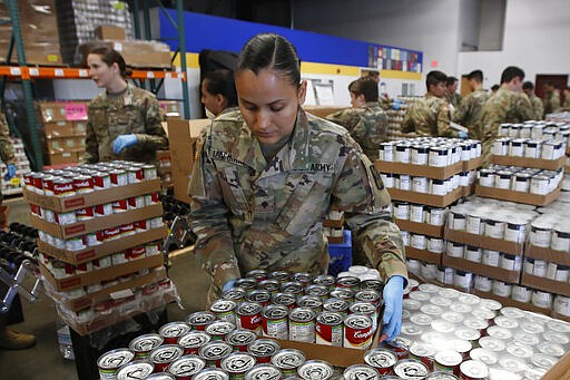 Specialist Yadira Izaguirre of the California National Guard picks up case of soup that will be packed with other food stuff supplies at the Sacramento Food Bank and Family Services in Sacramento, Calif., Saturday, March 21, 2020. Food banks have been hit hard by a shortage of volunteers due to the mandatory stay-at-home order caused by the coronavirus. Izaguirre and other members of the 115th Regional Support Group are supplementing food bank staff to ensure the food bank continues provide food to those in need. (AP Photo/Rich Pedroncelli)