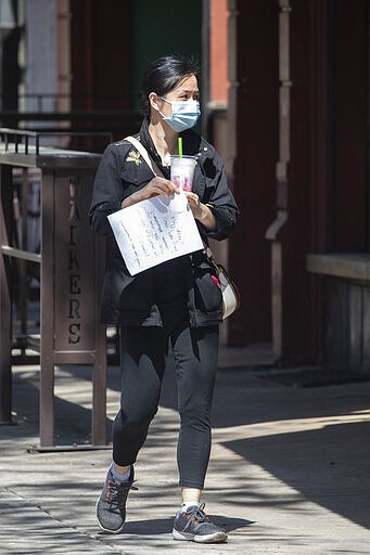 A woman wears a protective mask as she walks in downtown Athens, Ga. Friday, March 20, 2020. The city of Athens and Clarke County have pasted an ordinance requiring residents to shelter in place and is mandating social distancing to help slow the spread of COVID-19 virus. (AP Photo/John Bazemore)