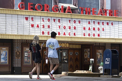 A couple walks past the marquee of the Georgia Theatre Friday, March 20, 2020, in Downton Athens, Ga. A note posted on the theatre's door says they are close and all shows are postponed. (AP Photo/John Bazemore)