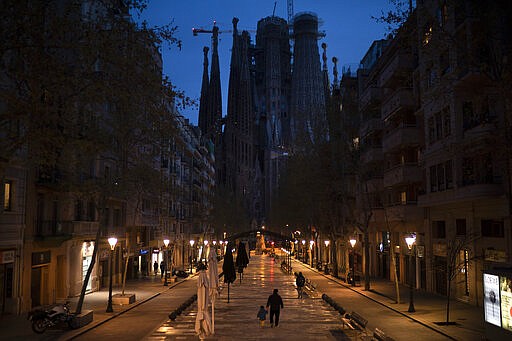 People walk past closed shops and restaurants near the La Sagrada Familia basilica, center, in Barcelona, Spain, March 18, 2020. (AP Photo/Felipe Dana)