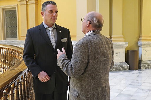 In this photo from Thursday, March 19, 2020, Kansas state Sen. Ty Masterson, left, R-Andover, confers with Rep. Ron Howard, R-Wichita, in the Statehouse rotunda in Topeka, Kan. Masterson and other Republicans are worried about the power Democratic Gov. Laura Kelly can wield in fighting the coronavirus pandemic now that she's ordered the state's schools closed for the rest of the semester. (AP Photo/John Hanna)