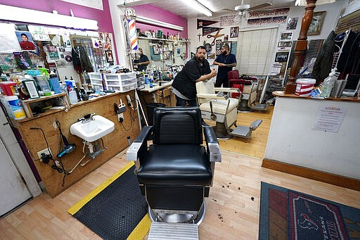 FILE - In this March 20, 2020 file photo, Carlos Vasquez, left, and his nephew R.J. Vasquez, wait for customers at their family's barber shop in Houston.  Reaction to the coronavirus, change came to the United States during the third week of March in 2020. It did not come immediately, though it came quite quickly. There was no explosion, no invasion other than a microscopic one that nobody could see.   (AP Photo/David J. Phillip, File)