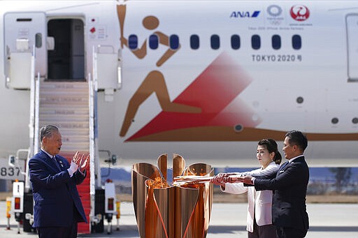 Three-time Olympic gold medalists Tadahiro Nomura, right, and Saori Yoshida light the torch as Tokyo 2020 Olympics chief Yoshiro Mori, left, watches during Olympic Flame Arrival Ceremony at Japan Air Self-Defense Force Matsushima Base in Higashimatsushima in Miyagi Prefecture, north of Tokyo Friday, March 20, 2020. The Olympic flame from Greece arrived in Japan even as the opening of the the Tokyo Games in four months is in doubt with more voices suggesting the games should to be postponed or canceled because of the worldwide virus pandemic. (AP Photo/Eugene Hoshiko)