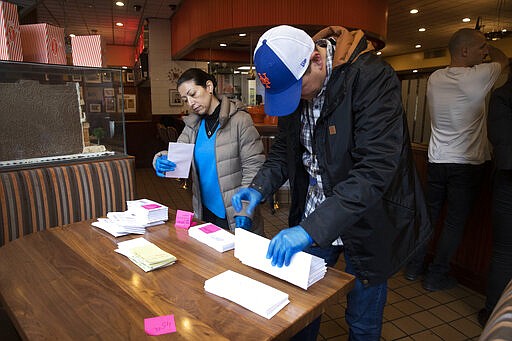 Employees of Junior's Restaurant sort paychecks for fellow workers who are picking them up, Thursday, March 19, 2020 in the Brooklyn borough of New York. The restaurant is closed temporarily due to the coronavirus. The company has laid off 650 of 850 employees at its four restaurants. (AP Photo/Mark Lennihan)