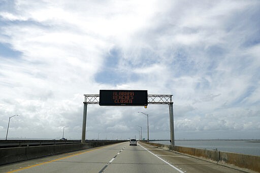 FILE - In this March 20, 2020, file photo a sign alerts commuters traveling westbound on Interstate 10 that Alabama beaches are closed in an effort to prevent the spread of the coronavirus in Spanish Fort, Ala. America has a history of unifying in trying times and rallying around the president, at least temporarily, in a crisis. But after years of division, there's little sign the coronavirus has punctured the nation&#146;s partisan bubbles. (AP Photo/Julio Cortez, File)