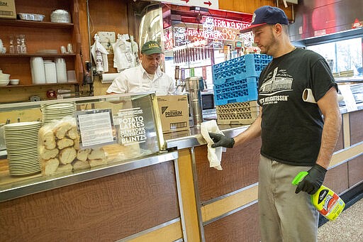 In this March 19, 2020 photo,  an employee disinfects the counter at Katz's Delicatessen on the Lower East Side of New York. The iconic eatery is only open for take out and delivery orders due to the coronavirus outbreak. (AP Photo/Mary Altaffer)