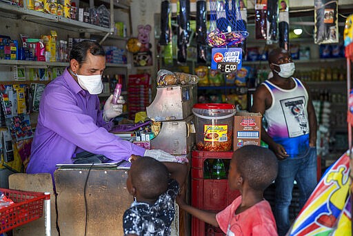 Iftikhar Ahmad, a Pakistani shopkeeper, is one of the very few wearing a mask in the Diepsloot township north of Johannesburg, South Africa, Saturday March 21, 2020. At right is Prince, a Nigerian money changer.  For most people the virus causes only mild or moderate symptoms. For others it can cause more severe illness, especially in older adults and people with existing health problems. (AP Photo/Jerome Delay)