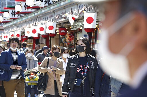 Visitors wearing face masks walk through Nakamise alley at Asakusa in Tokyo, Friday, March 20, 2020. For most people, the new coronavirus causes only mild or moderate symptoms. For some it can cause more severe illness. (AP Photo/Koji Sasahara)