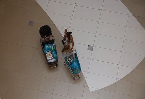 CAPTION CORRECTS THE DATE In a normally crowded shopping mall a couple push their shopping trolleys across the centre court at the Sandton City shopping mall in Johannesburg, South Africa, Saturday March 21, 2020. There is a noticeable drop in crowds of shoppers at malls due the spread of the coronavirus. For most people the new coronavirus causes mild or moderate symptoms, but for some, especially older adults and people with existing health problems, it can cause more severe illness, including pneumonia. (AP Photo/Denis Farrell)