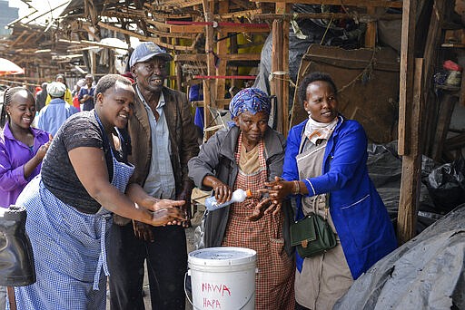 Street traders wash their hands as they watch Kenyan Health Ministry officials spraying disinfectant to control the spread of the new coronavirus, in the Gikomba outdoor street market in the capital Nairobi, Kenya Saturday, March 21, 2020. For most people, the new coronavirus causes only mild or moderate symptoms such as fever and cough and the vast majority recover in 2-6 weeks but for some, especially older adults and people with existing health issues, the virus that causes COVID-19 can result in more severe illness, including pneumonia. (AP Photo/John Muchucha)