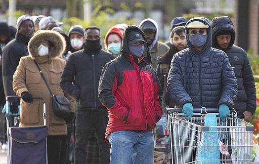 People queue outside a large supermarket store, a day after the government unveiled an emergency package aimed at protecting workers' jobs and wages as they face hardship in the fight against the coronavirus pandemic, in London, Saturday March 21, 2020.  For some people the COVID-19 coronavirus causes mild or moderate symptoms, but for some it causes severe illness. (Dominic Lipinski / PA via AP)