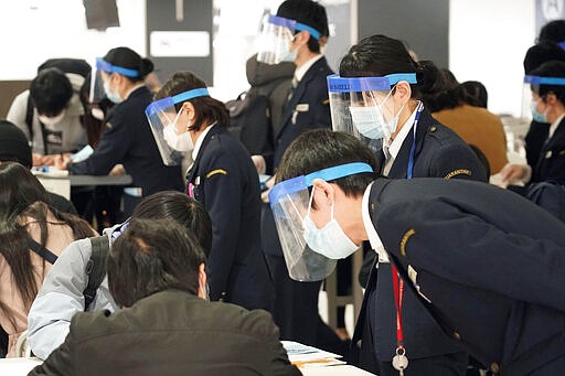 Quarantine staff members wear face masks and shields as passengers arriving from Germany fill a form at Narita international airport in Narita, near Tokyo Saturday, March 21, 2020. For most people, the new coronavirus causes only mild or moderate symptoms. For some it can cause more severe illness. (Kyodo News via AP)