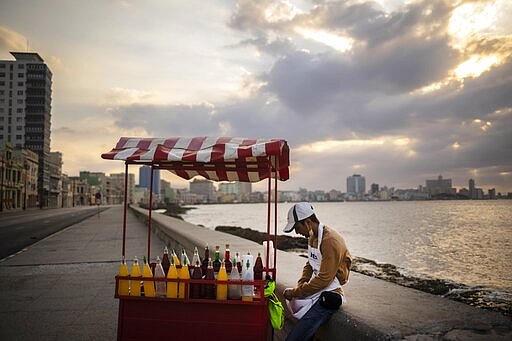 A slushy street vendor, who uses a protective face mask when he has customers as a precaution against the spread of the new coronavirus, waits for them along the seawall, normally bustling with pedestrians, in Havana, Cuba, Friday, March 20, 2020. (AP Photo/Ramon Espinosa)