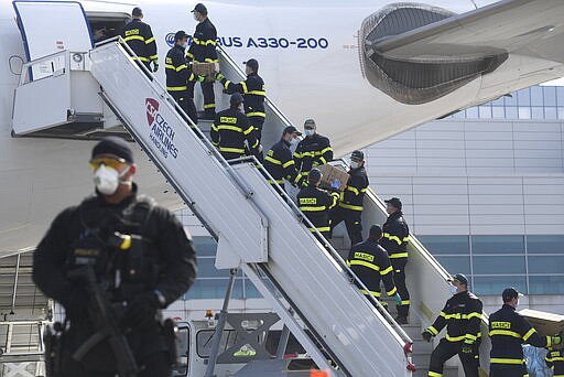 A police officer holds a gun as firefighters unload an airplane after its arrival at the Vaclav Havel Airport in Prague, Friday, March 20, 2020. The airplane brought medical aid and protective materials against coronavirus from China. (Michal Kamaryt/CTK via AP)