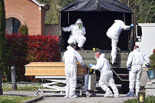 Coffins are downloaded at the Ferrara cemetery, northern Italy, from a military convoy coming from Bergamo, a city at the epicenter of the coronavirus outbreak in northern Italy, Saturday, March 21, 2020. The Bergamo's mortuary reached its maximum capacity and many victims of the epidemic are being cremated in other cities.  For most people, the new coronavirus causes only mild or moderate symptoms. For some it can cause more severe illness, especially in older adults and people with existing health problems. (Massimo Paolone/LaPresse via AP)