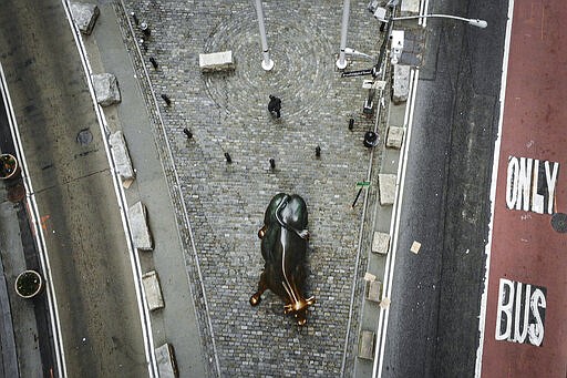 A lone pedestrian walks down Broadway past the Charging Bull statue as COVID-19 concerns empty a typically bustling downtown area, Saturday, March 21, 2020, in New York. New York Gov. Andrew Cuomo announced sweeping orders Friday that will severely restrict gatherings of any size for the state's more than 19 million residents and will require workers in nonessential businesses to stay home. (AP Photo/John Minchillo)