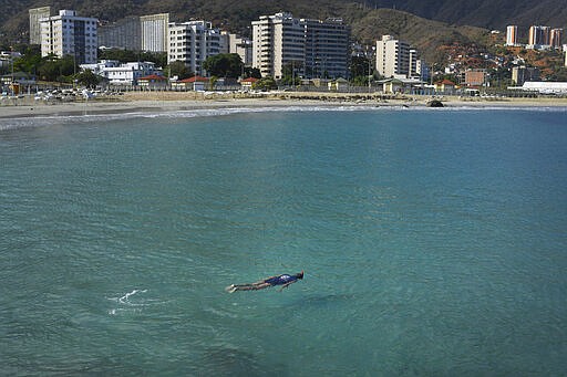 A man swims in the normally crowded popular beach Los Corales, in La Guaira, Venezuela, Saturday, March 21, 2020. Most people are staying home after nonessential activities were cancelled due to the COVID-19 pandemic. (AP Photo/Matias Delacroix)