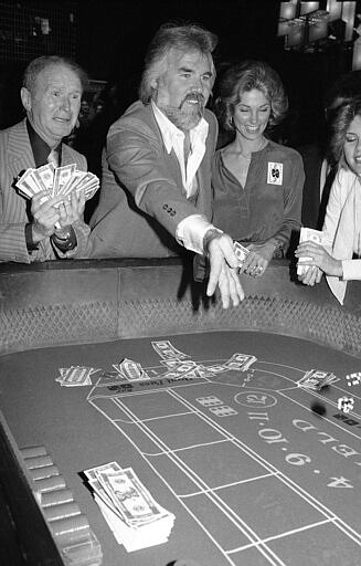 FILE - In this March 22, 1979 file photo,   Kenny Rogers, center, rolls the dice at Regine's in New York.   Rogers, who embodied &#147;The Gambler&#148; persona and whose musical career spanned jazz, folk, country and pop, has died at 81. A representative says Rogers died at home in Georgia on Friday, March 20, 2020.  (AP Photo/Richard Drew, File)