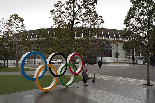 A woman pauses for photos next to the Olympic rings near the New National Stadium in Tokyo, Monday, March 23, 2020. The IOC will take up to four weeks to consider postponing the Tokyo Olympics amid mounting criticism of its handling of the coronavirus crisis that now includes a call for delay from the leader of track and field, the biggest sport at the games. (AP Photo/Jae C. Hong)