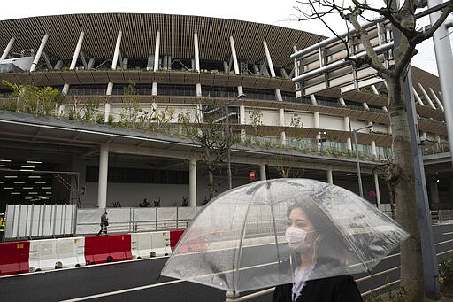 A woman walks past the New National Stadium, a venue for the opening and closing ceremonies at the Tokyo 2020 Olympics, in Tokyo, Monday, March 23, 2020. The IOC will take up to four weeks to consider postponing the Tokyo Olympics amid mounting criticism of its handling of the coronavirus crisis that now includes a call for delay from the leader of track and field, the biggest sport at the games. (AP Photo/Jae C. Hong)