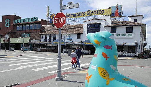 A couple walk along the deserted Fisherman's Wharf area Sunday, March 22, 2020, in San Francisco. Some 40 million Californians are coping with their first weekend under a statewide order requiring them to stay at home to help curb the spread of the coronavirus. (AP Photo/Ben Margot)