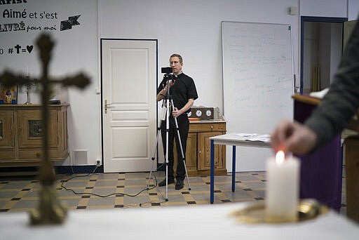 Priest Philippe Rochas of the St. Vincent de Paul church prepares a livestream of Sunday mass in Marseille, southern France, Sunday, March 22, 2020. As mass gatherings are forbidden due to measures to prevent the spread of COVID- 19, priests are using technology to reach worshippers forced to stay at home. For most people, the new coronavirus causes only mild or moderate symptoms. (AP Photo/Daniel Cole)