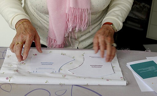 In this photo taken on Thursday, March 19, 2020, Magda Leonard, lays out a pattern for a face mask, meant to help protect from the spread of COVID-19, that she produced on her sewing machine at home in Edegem, Belgium. Leonard is making masks, along with her daughter, for family and friends and hopes to be able to produce enough to deliver to caregivers and local doctors. Belgium currently has a need for the masks due to a shortage in supply of industrially made masks. For most people, the new coronavirus causes only mild or moderate symptoms, such as fever and cough. For some, especially older adults and people with existing health problems, it can cause more severe illness, including pneumonia. (Gerd Moyson via AP)