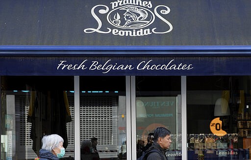 A woman in a protective mask walks by a Belgian chocolate shop in the center of Antwerp, Belgium, Saturday, March 14, 2020. Belgium has closed schools, restaurants and bars, as as well as cancelled sporting and cultural events in an effort to contain the spread of the coronavirus. For most people, the new coronavirus causes only mild or moderate symptoms, such as fever and cough. For some, especially older adults and people with existing health problems, it can cause more severe illness, including pneumonia. (AP Photo/Virginia Mayo)