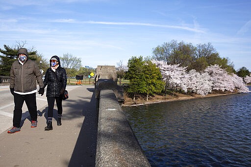 Dave Anderson, left, and Panadda Harrington, both of Reston, Va., walk hand-in-gloved-hand while wearing cloth face masks as they visit the tidal basin to see the cherry blossom trees in full bloom, Sunday, March 22, 2020, in Washington. &quot;We walk everyday,&quot; says Harrington, &quot;and cabin fever pushed us out to see the blossoms. We didn't think it would be as crowded as usual and it's not. We would only have been concerned about coronavirus if it had been very crowded.&quot;  (AP Photo/Jacquelyn Martin)