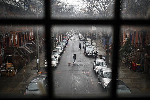 A pedestrian walks their dog through a quiet street, Tuesday, March 17, 2020, in the Brooklyn borough of New York. As of Sunday, nearly 2,000 people with the virus have been hospitalized in the state of New York, and 114 have died, officials said. More than 15,000 have tested positive statewide, including 9,000 in New York City.  (AP Photo/John Minchillo)