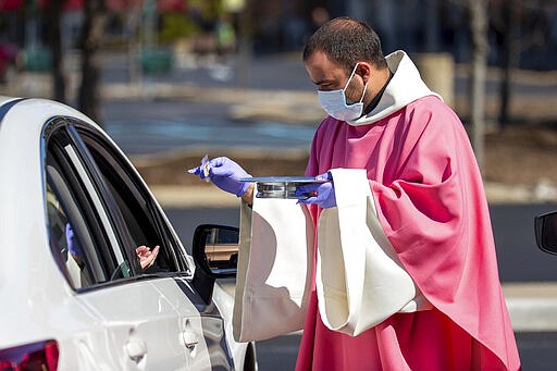 Rev. William A. Mentz, pastor of the Scranton, Pa. based St. Francis and Clare Progressive Catholic Church, wears a mask and gloves while distributing prepackaged communion to the faithful attending mass while sitting in their cars in a parking lot at the Shoppes at Montage in Moosic, Pa. on Sunday, March 22, 2020. The Progressive Catholic Church is a small denomination operating independently of the Roman Catholic Church. Other Catholic churches in the Scranton area suspended the celebration of mass to help control the spread of COVID-19. (Christopher Dolan/The Times-Tribune via AP)