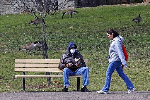 A man sits on a park bench as a woman walks past in West Park on the Northside of Pittsburgh, Sunday, March 22, 2020. (AP Photo/Gene J. Puskar)