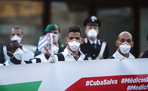 Medics and paramedics from Cuba pose upon arrival at the Malpensa airport of Milan, Italy, Sunday, March 22, 2020. 53 doctors and nurses from Cuba arrived in Milan to help with coronavirus treatment in Crema. For most people, the new coronavirus causes only mild or moderate symptoms. For some it can cause more severe illness, especially in older adults and people with existing health problems. (AP Photo/Antonio Calanni)