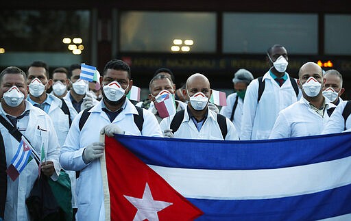 Medics and paramedics from Cuba pose upon arrival at the Malpensa airport of Milan, Italy, Sunday, March 22, 2020. 53 doctors and paramedics from Cuba arrived in Milan to help with coronavirus treatment in Crema. For most people, the new coronavirus causes only mild or moderate symptoms. For some it can cause more severe illness, especially in older adults and people with existing health problems. (AP Photo/Antonio Calanni)