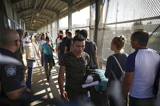 FILE - In this Aug. 2, 2019, file photo, migrants return to Mexico as other migrants line up on their way to request asylum in the U.S., at the foot of the Puerta Mexico bridge in Matamoros, Mexico, that crosses into Brownsville, Texas. One by one, asylum-seekers from El Salvador and Honduras who are waiting in Mexico for court hearings in the United States appeared before an immigration judge to explain why, after months of effort, they couldn't find an attorney. Only 5.3% of asylum-seekers subject to the Migrant Protection Protocols, as the &quot;Remain in Mexico&quot; policy is officially known, had lawyers through the end of January, compared with 85% for asylum-seekers nationwide, according to Syracuse University's Transactional Records Access Clearinghouse. (AP Photo/Emilio Espejel, File)