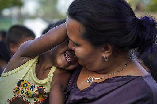 FILE - In this Aug. 30, 2019 file photo, a Honduran mother plays with her son as they wait in line to get a meal in an encampment near the Gateway International Bridge in Matamoros, Mexico. One by one, asylum-seekers from El Salvador and Honduras who are waiting in Mexico for court hearings in the United States appeared before an immigration judge to explain why, after months of effort, they couldn't find an attorney.  (AP Photo/Veronica G. Cardenas, File)