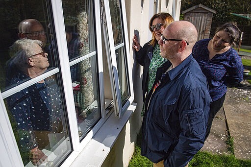 76-year old Olive Trotman, left, is visited on Mother's Day by her son Mark, his wife Denise and his sister Kelly, in Napton, England, Sunday March 22, 2020. Olive suffers from a pulmonary disease and is taking the precaution of communicating at a safe distance or through a glass window, to limit the potential spread of COVID-19 coronavirus.  Sunday is Mother&#146;s Day in Britain and the government has a stark message for millions of citizens, that visiting your mom could kill her as for older adults and people with existing health problems, the virus can cause severe illness, including pneumonia. (Jacob King / PA via AP)