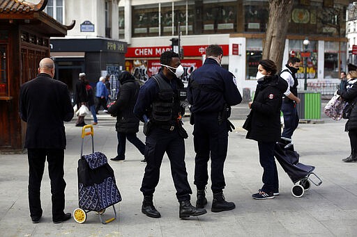 Police officers check people at the entrance of the open air market of Belleville, in Paris, Friday, March 20, 2020. French President Emmanuel Macron said that for 15 days starting at noon on Tuesday, people will be allowed to leave the place they live only for necessary activities such as shopping for food, going to work or taking a walk. For most people, the new coronavirus causes only mild or moderate symptoms. For some it can cause more severe illness, especially in older adults and people with existing health problems. (AP Photo/Thibault Camus)
