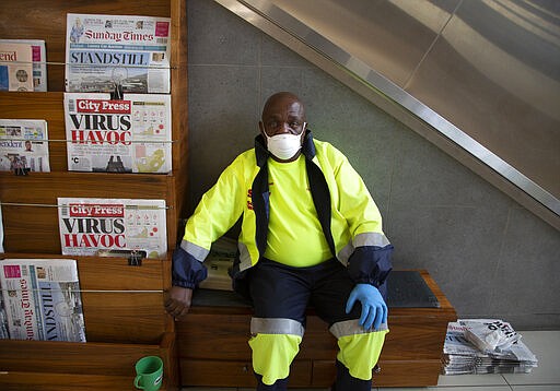 A masked newspaper seller waits to make a sale in the virtually empty Rosebank Mall in Johannesburg, Sunday, March 22, 2020. There is a noticeable drop in crowds of shoppers at malls due the spread of the coronavirus. For most people the virus causes only mild or moderate symptoms . For others it can cause more severe illness, especially in older adults and people with existing health problems. (AP Photo/Denis Farrell)