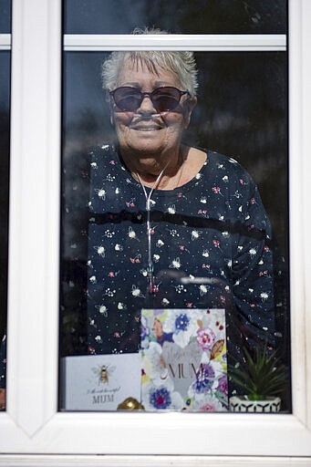 76-year old Olive Trotman, looks out from her home during as she is visited on Mother's Day by her son Mark, his wife Denise and his sister Kelly, in Napton, England, Sunday March 22, 2020. Olive suffers from a pulmonary disease and is taking the precaution of communicating at a safe distance or through a glass window, to limit the potential spread of COVID-19 coronavirus.  Sunday is Mother&#146;s Day in Britain and the government has a stark message for millions of citizens, that visiting your mom could kill her as for older adults and people with existing health problems, the virus can cause severe illness, including pneumonia. (Jacob King / PA via AP)