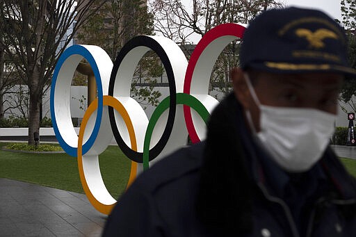 A security guard walks past the Olympic rings near the New National Stadium in Tokyo, Monday, March 23, 2020. The IOC will take up to four weeks to consider postponing the Tokyo Olympics amid mounting criticism of its handling of the coronavirus crisis that now includes a call for delay from the leader of track and field, the biggest sport at the games. (AP Photo/Jae C. Hong)