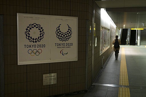 A commuter leaves a train station adorned with posters promoting the Tokyo 2020 Olympics in Tokyo, Monday, March 23, 2020. The IOC will take up to four weeks to consider postponing the Tokyo Olympics amid mounting criticism of its handling of the coronavirus crisis that now includes a call for delay from the leader of track and field, the biggest sport at the games. (AP Photo/Jae C. Hong)